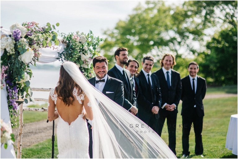 A groom smiling at the bride during an outdoor wedding ceremony.