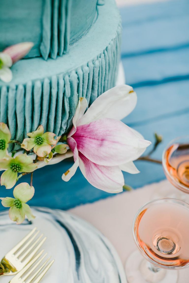 A pink flower and green buds beside a cake on a blue table.