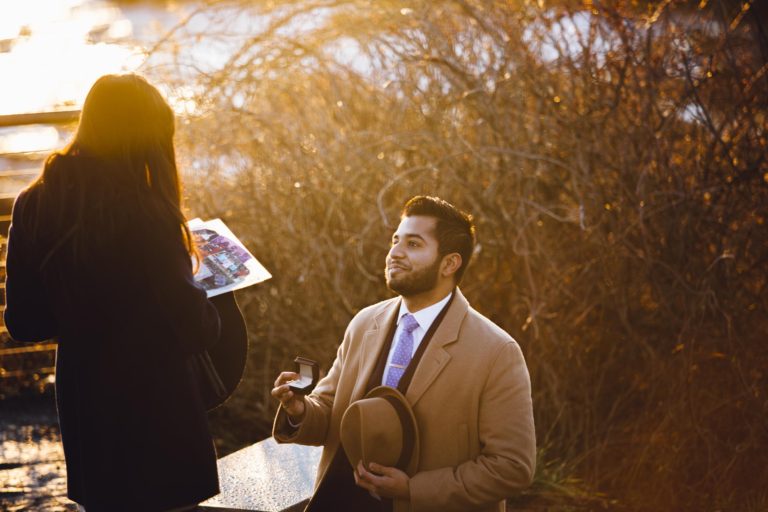 Man in brown coat holding a hat and a painting outdoors.