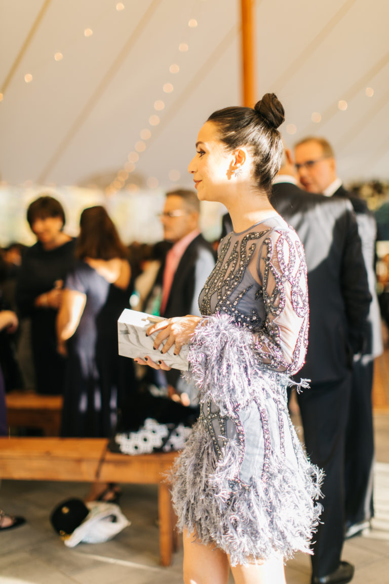 A woman in a detailed lace dress holding a clutch in a formal setting.